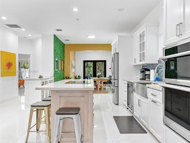 kitchen featuring white cabinetry, tasteful backsplash, a breakfast bar, stainless steel appliances, and beverage cooler