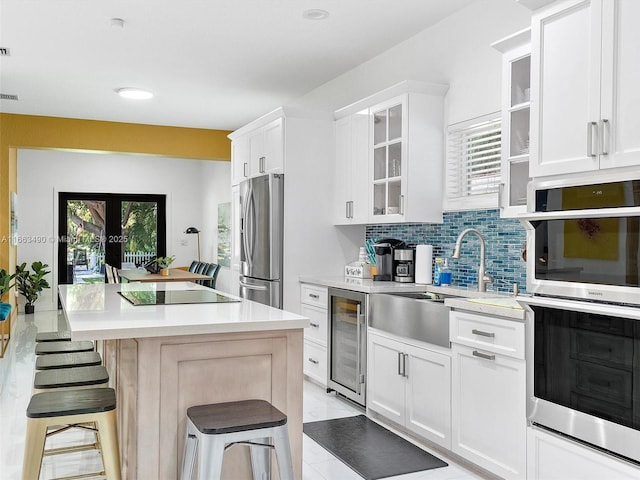 kitchen featuring light countertops, appliances with stainless steel finishes, white cabinets, beverage cooler, and a kitchen breakfast bar