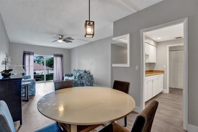 dining area featuring light wood-type flooring, ceiling fan, and a textured ceiling