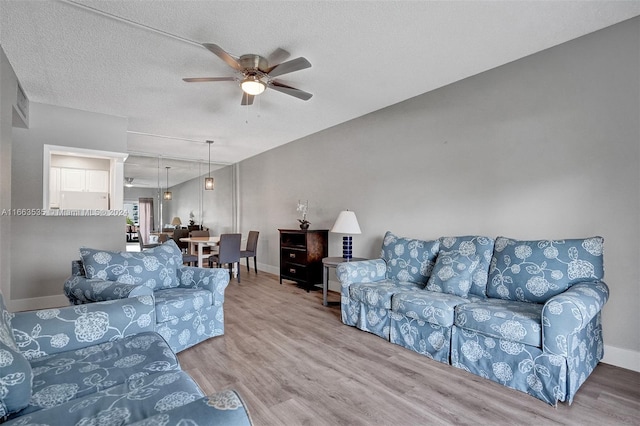 living room with a textured ceiling, ceiling fan, and hardwood / wood-style flooring