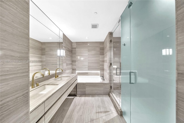 bathroom featuring tile patterned flooring, shower with separate bathtub, vanity, and tile walls