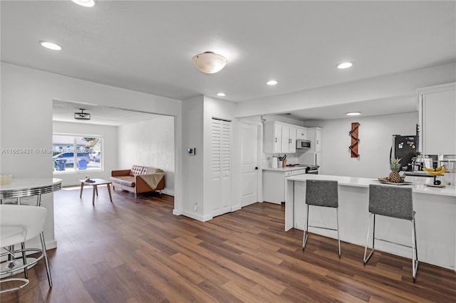 kitchen with dark wood-type flooring, white cabinets, kitchen peninsula, a kitchen bar, and refrigerator