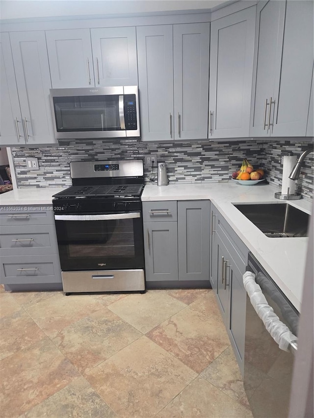 kitchen with appliances with stainless steel finishes, sink, gray cabinets, and backsplash