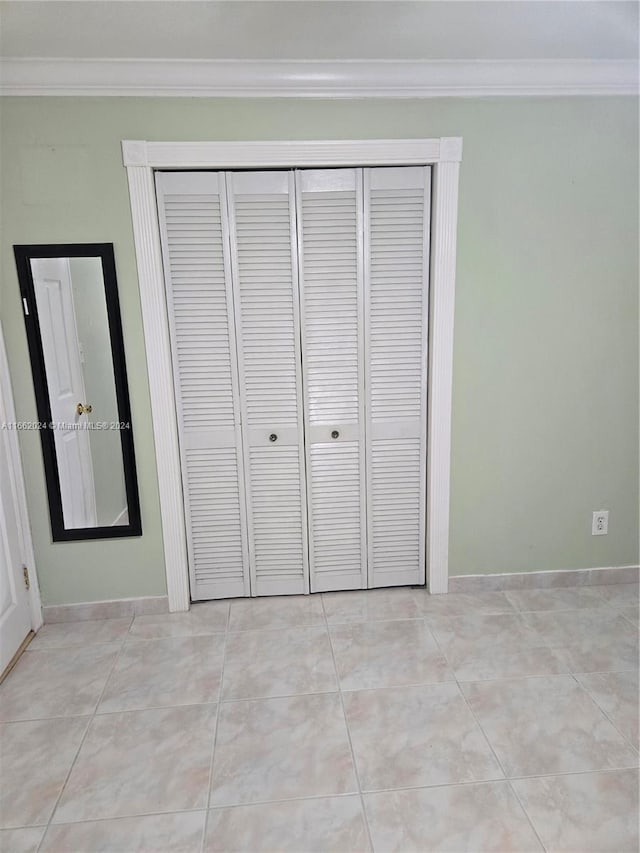 unfurnished bedroom featuring a closet, crown molding, and light tile patterned flooring