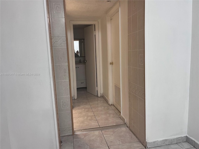 hall featuring a textured ceiling, tile walls, sink, and light tile patterned floors