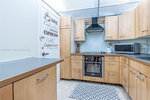 kitchen featuring pendant lighting, wall chimney range hood, oven, light brown cabinets, and light tile patterned floors