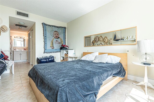 bedroom featuring ensuite bath, a textured ceiling, and light tile patterned flooring