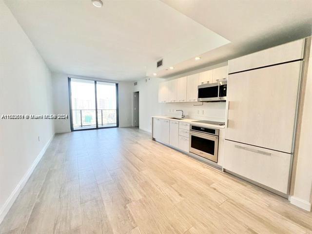 45 SW 9th St Unit 3009, Miami, FL 33130 - kitchen featuring appliances with stainless steel finishes, a sink, white cabinets, baseboards, and light wood-style flooring