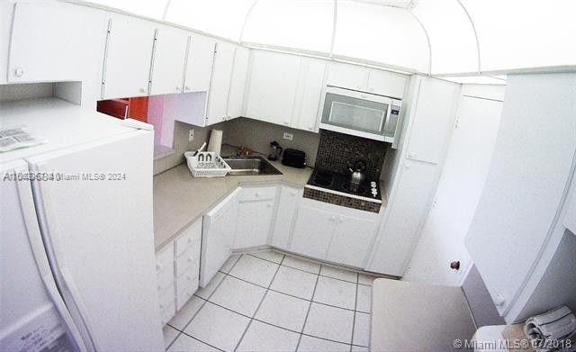 kitchen with black electric cooktop, white cabinets, white refrigerator, light tile patterned floors, and sink