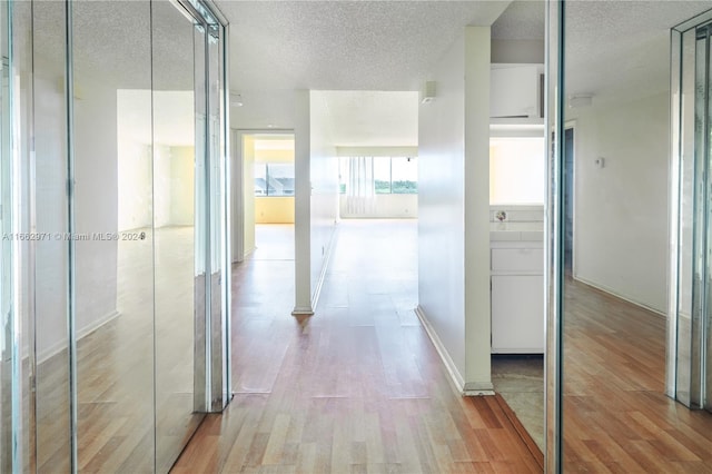 hall with a textured ceiling and light hardwood / wood-style flooring