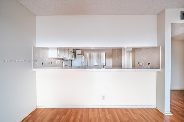 kitchen with light wood-type flooring, a textured ceiling, white appliances, and tasteful backsplash