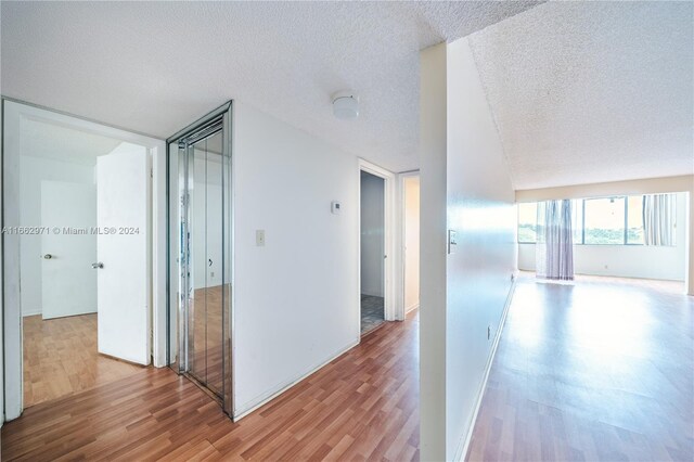 corridor with a textured ceiling and light wood-type flooring