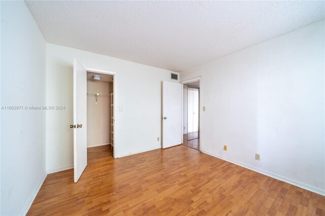 unfurnished bedroom featuring a textured ceiling, light wood-type flooring, a closet, and a walk in closet