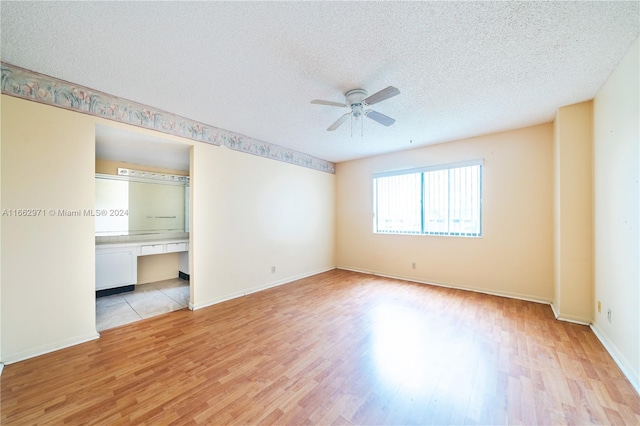 unfurnished room featuring a textured ceiling, light hardwood / wood-style floors, ceiling fan, and built in desk