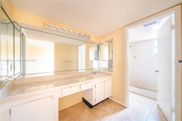 bathroom with a textured ceiling, a tile shower, tile patterned flooring, and vanity