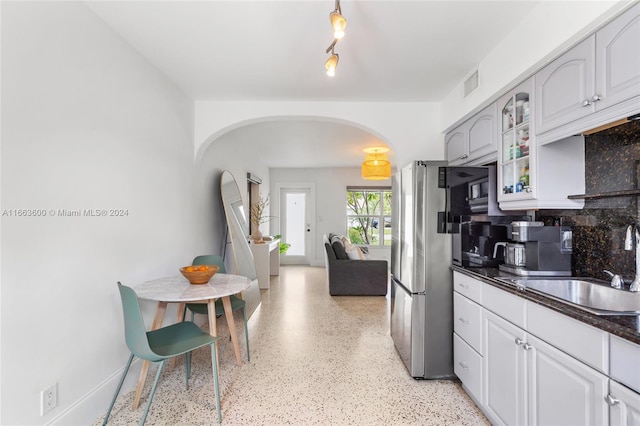 kitchen featuring sink, stainless steel fridge, white cabinetry, and decorative backsplash