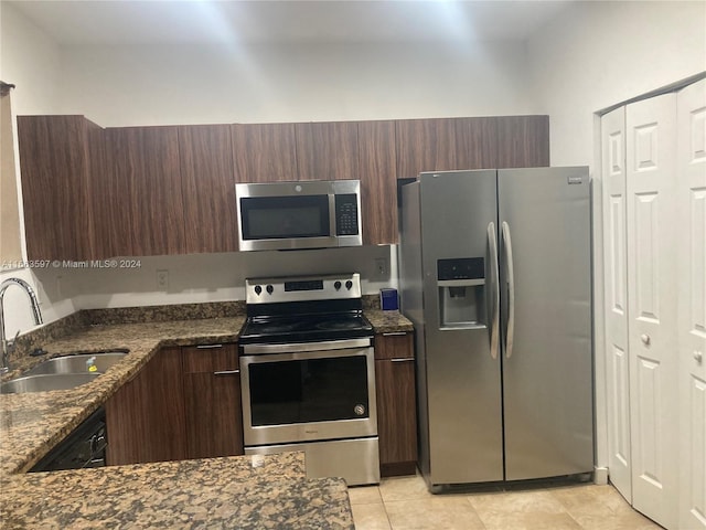 kitchen with dark stone counters, sink, appliances with stainless steel finishes, dark brown cabinets, and light tile patterned flooring