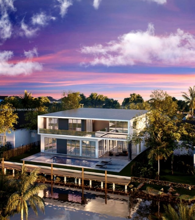 back house at dusk featuring a balcony, a swimming pool, and a patio