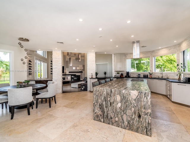 kitchen with sink, white cabinets, a kitchen island, and dark stone countertops