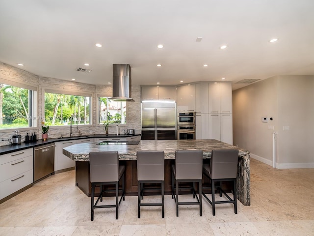 kitchen with a spacious island, dark stone counters, a kitchen bar, range hood, and stainless steel appliances