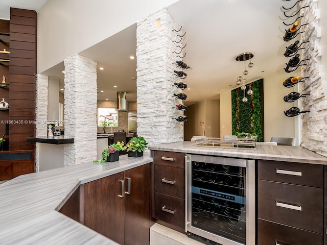 bar with dark brown cabinets, beverage cooler, and ornate columns