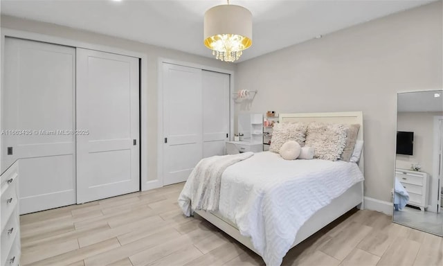 bedroom featuring light wood-type flooring, a notable chandelier, and two closets