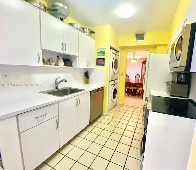 kitchen featuring sink, stainless steel appliances, stacked washer / drying machine, white cabinets, and light tile patterned flooring