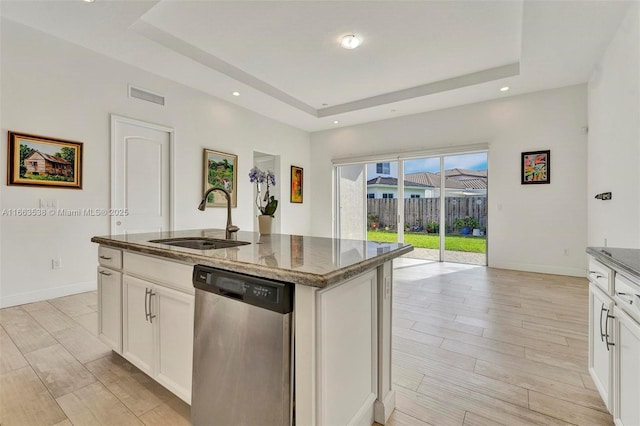 kitchen with dishwasher, a raised ceiling, sink, an island with sink, and white cabinetry