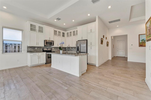 kitchen featuring white cabinets, a kitchen island with sink, appliances with stainless steel finishes, and dark stone counters