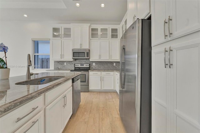 kitchen with appliances with stainless steel finishes, light wood-type flooring, light stone counters, sink, and white cabinets