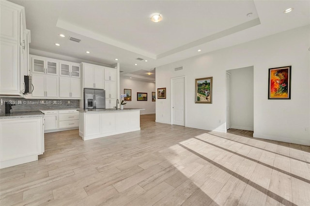 kitchen with stainless steel fridge, a raised ceiling, and a kitchen island with sink