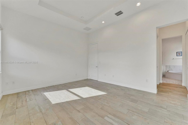 empty room with light wood-type flooring and a tray ceiling