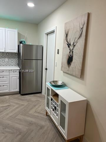 kitchen with tasteful backsplash, stainless steel fridge, light parquet flooring, and white cabinets