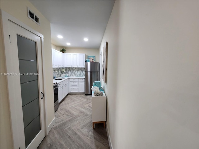 kitchen featuring light parquet floors, sink, tasteful backsplash, white cabinetry, and stainless steel appliances