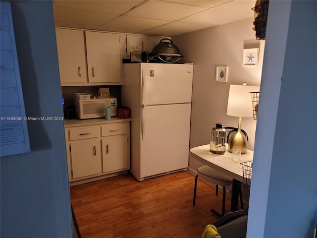 kitchen with white cabinets, a paneled ceiling, light wood-type flooring, and white appliances