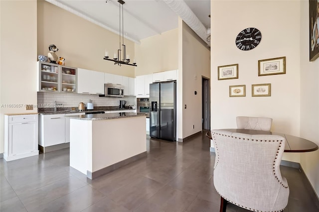 kitchen with white cabinets, pendant lighting, appliances with stainless steel finishes, a towering ceiling, and tasteful backsplash