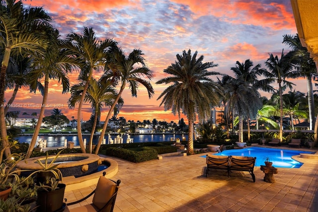 pool at dusk with a patio and a water view