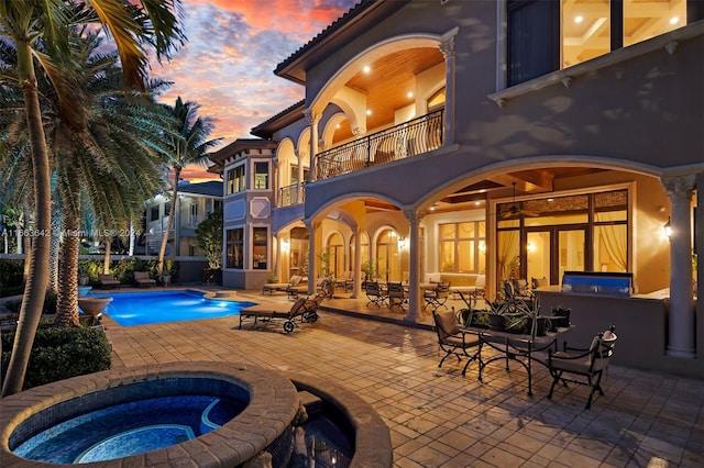 pool at dusk featuring an in ground hot tub and a patio area