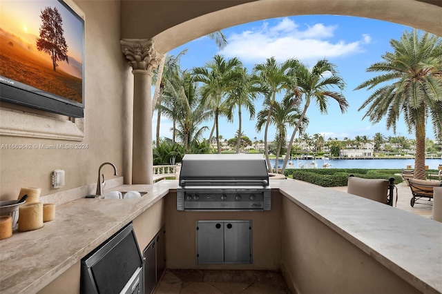 view of patio / terrace featuring a water view, exterior kitchen, sink, and a grill