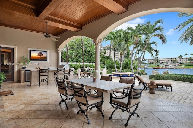 view of patio with a bar, a water view, area for grilling, and ceiling fan