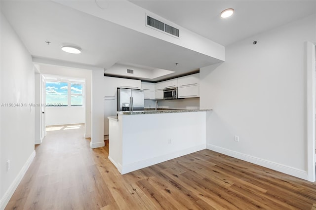 kitchen featuring light hardwood / wood-style floors, white cabinetry, kitchen peninsula, stainless steel appliances, and stone countertops