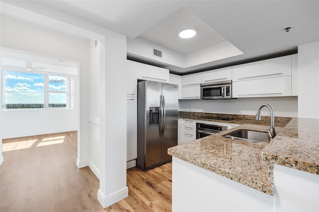 kitchen featuring white cabinetry, light stone countertops, stainless steel appliances, light hardwood / wood-style flooring, and sink