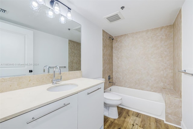 full bathroom with wood-type flooring, vanity, tiled shower / bath combo, and toilet