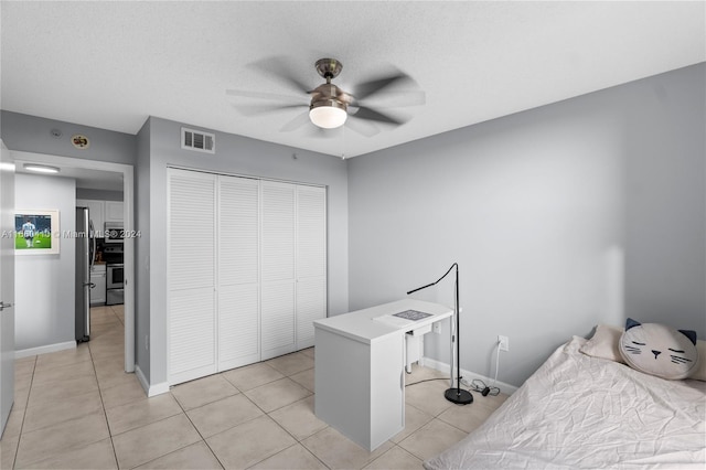 bedroom featuring light tile patterned floors, stainless steel refrigerator, a closet, and ceiling fan