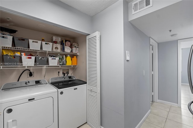 clothes washing area with washer and dryer, a textured ceiling, and light tile patterned flooring