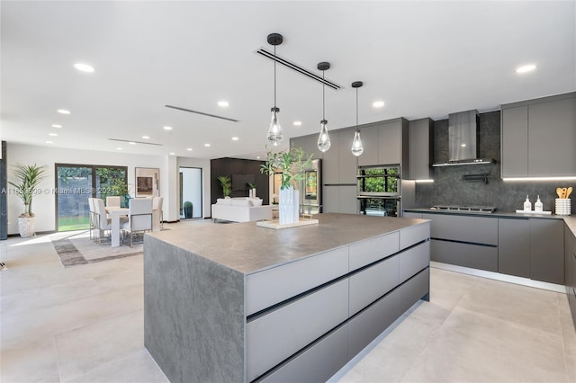 kitchen featuring stainless steel gas cooktop, a large island, wall chimney range hood, and gray cabinets