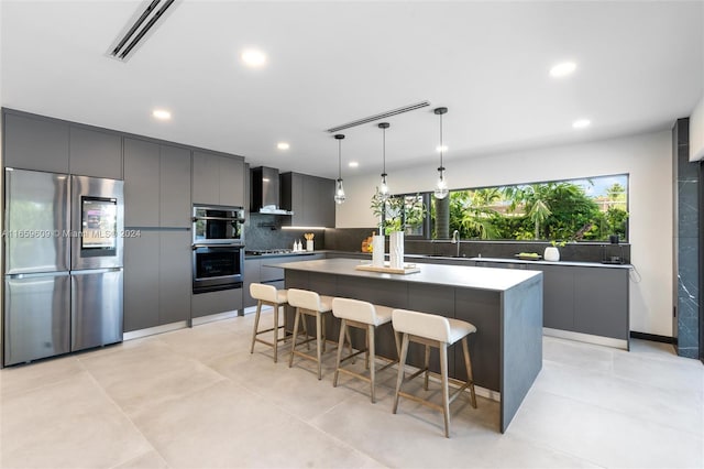 kitchen featuring appliances with stainless steel finishes, a kitchen island, decorative light fixtures, sink, and wall chimney range hood