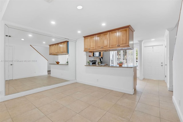 kitchen featuring light tile patterned floors, sink, kitchen peninsula, appliances with stainless steel finishes, and dark stone countertops