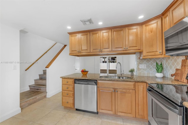 kitchen featuring tasteful backsplash, sink, stone counters, appliances with stainless steel finishes, and light tile patterned floors