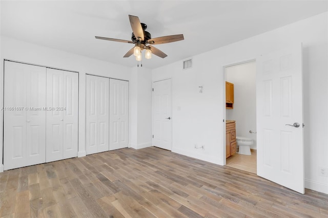 unfurnished bedroom featuring two closets, light wood-type flooring, ensuite bath, and ceiling fan